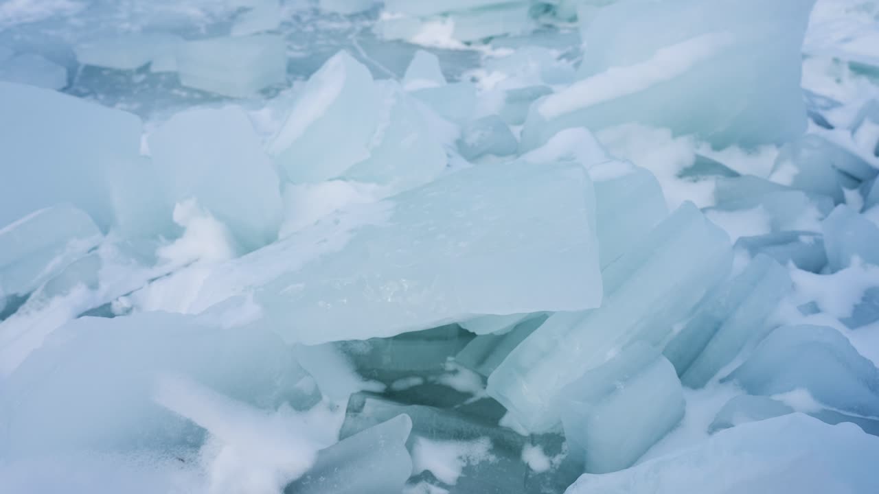 Primo piano di lastre di ghiaccio blu traslucide accumulate su acqua ghiacciata, creando una texture invernale astratta. Suggerisce ghiaccio sottile e fragile, pericolo di freddo e un'atmosfera di disgelo climatico con spazio per il testo.
