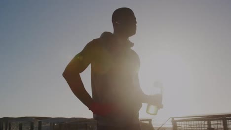 Colorful-spots-of-light-against-african-american-fit-man-drinking-water-at-the-beach