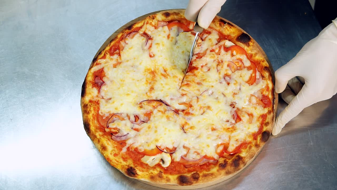 Cutting Italian pizza into slices on the table. Round pizza cutter. View from above. Cook's hands in white gloves