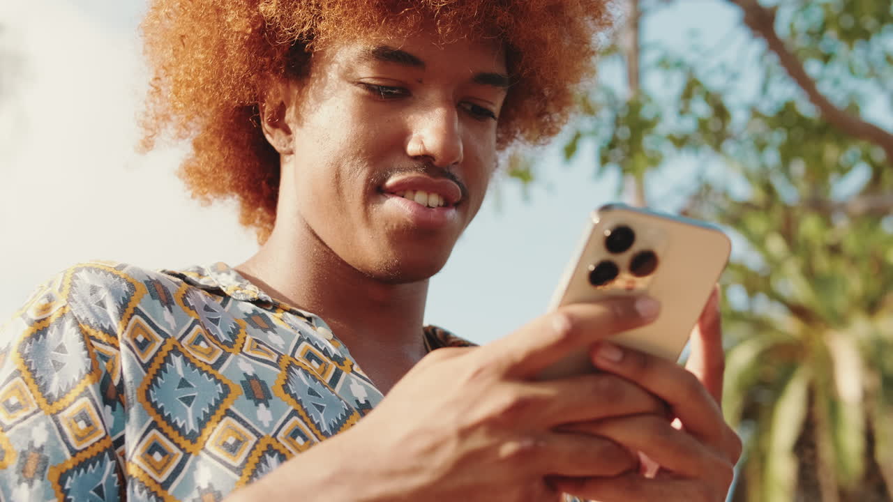 Jeune homme aux cheveux bouclés utilisant un smartphone à l’extérieur