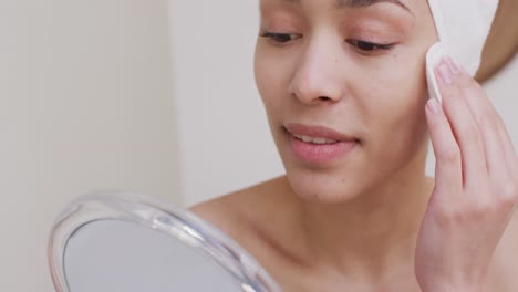 mujer biracial con una toalla lavándose la cara en el baño