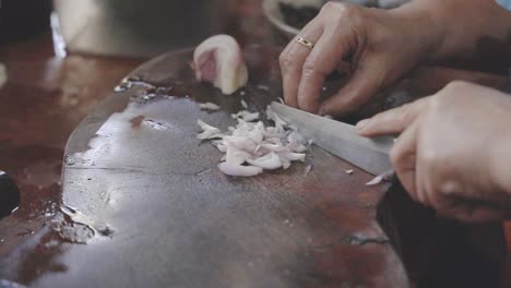 almohadilla de cocina serie tailandesa: cámara lenta, mano del chef de primer plano rebanando la chalota en rodajas finas en una tabla de cortar de madera en la tienda de comida callejera tailandesa