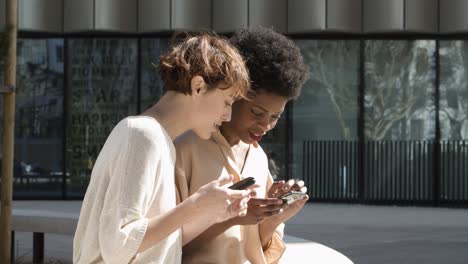 Side-view-of-cheerful-friends-browsing-internet-via-smartphones