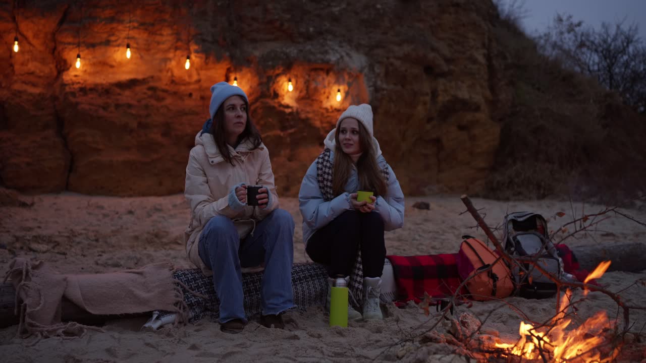 Two friends enjoying a campfire on the beach at night.