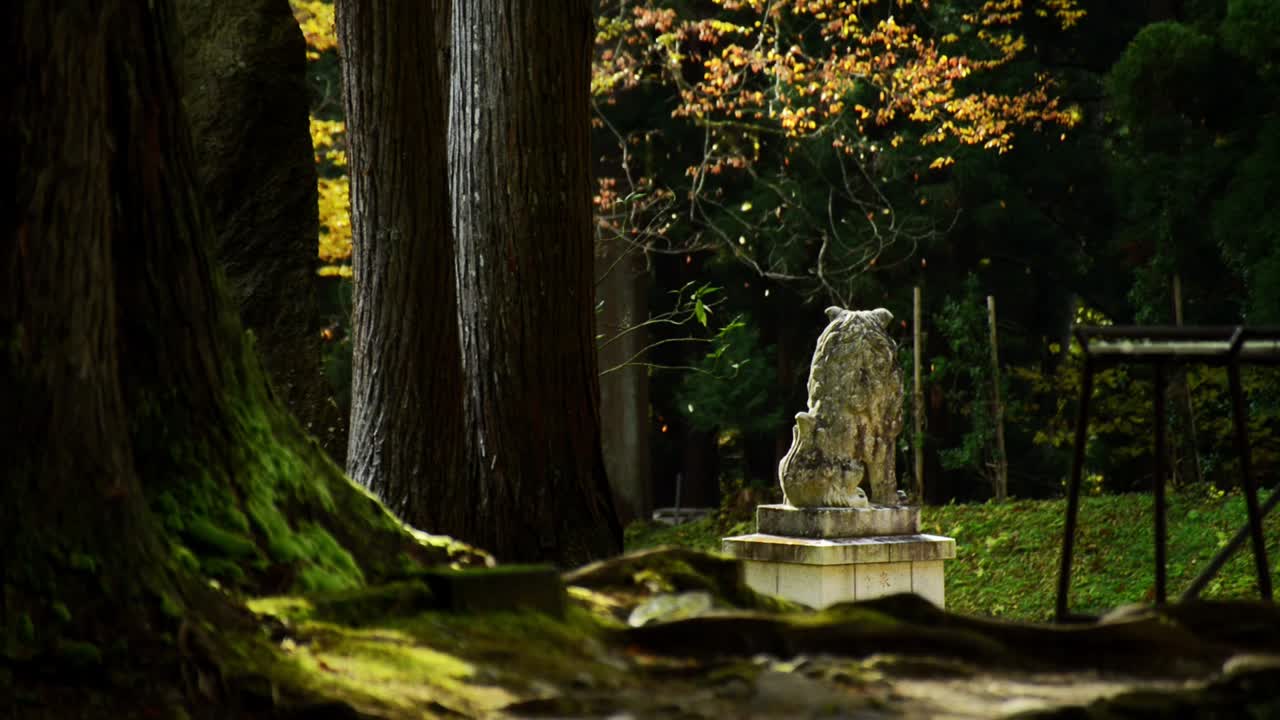 Foglie autunnali che cadono su una statua di leone-cane Komainu in un tempio giapponese in una pineta