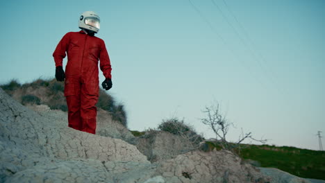 astronaut with orange suit and helmet walks on the rocks of a hostile planet