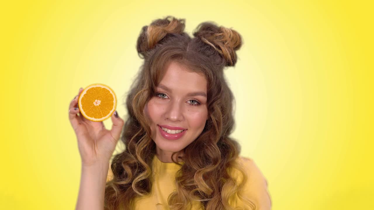 스타일링 포즈의 아름다운 젊은 소녀는 오렌지색 눈살을 이고 카메라를 바라보며 미소 짓습니다.