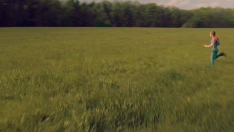 young boy child running fast over meadow with backpack