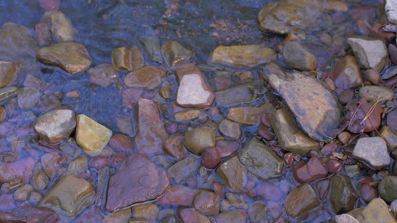 Increspature e riflessi lungo il bordo di un piccolo ruscello accanto a piccole rocce colorate