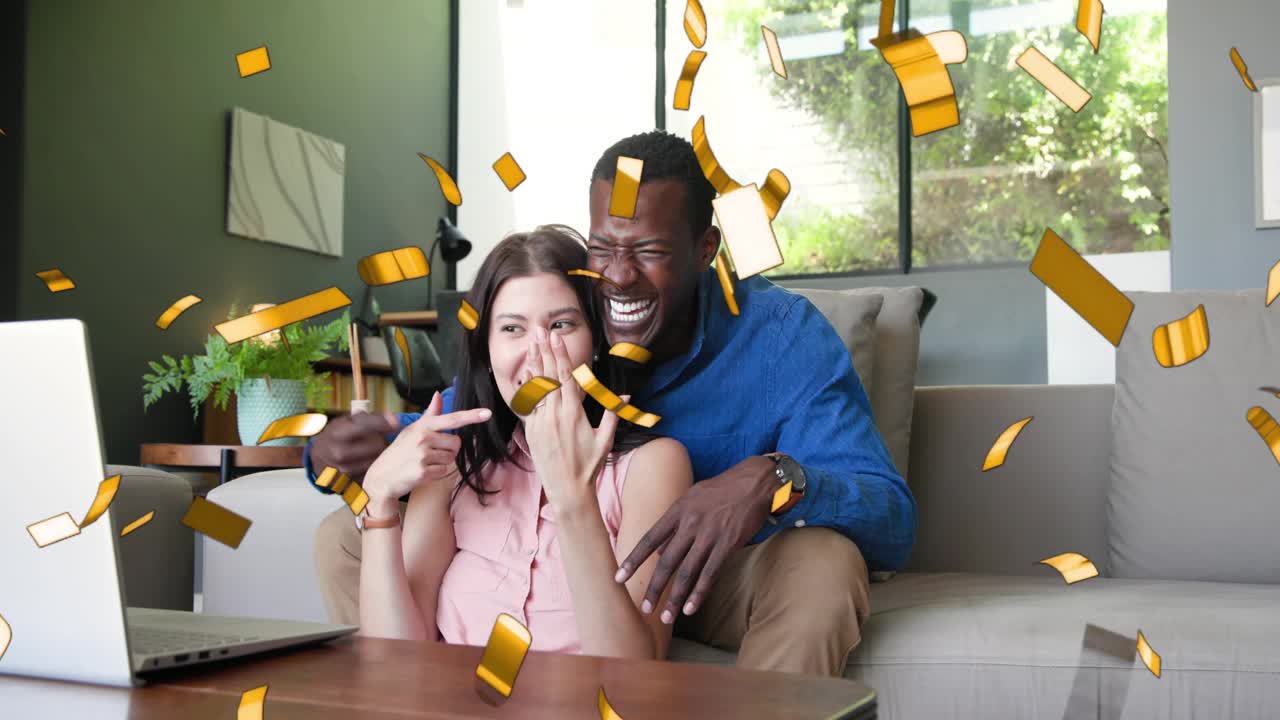 Couple getting virtual call causing confetti overlay, cheering while waving and laughing at laptop