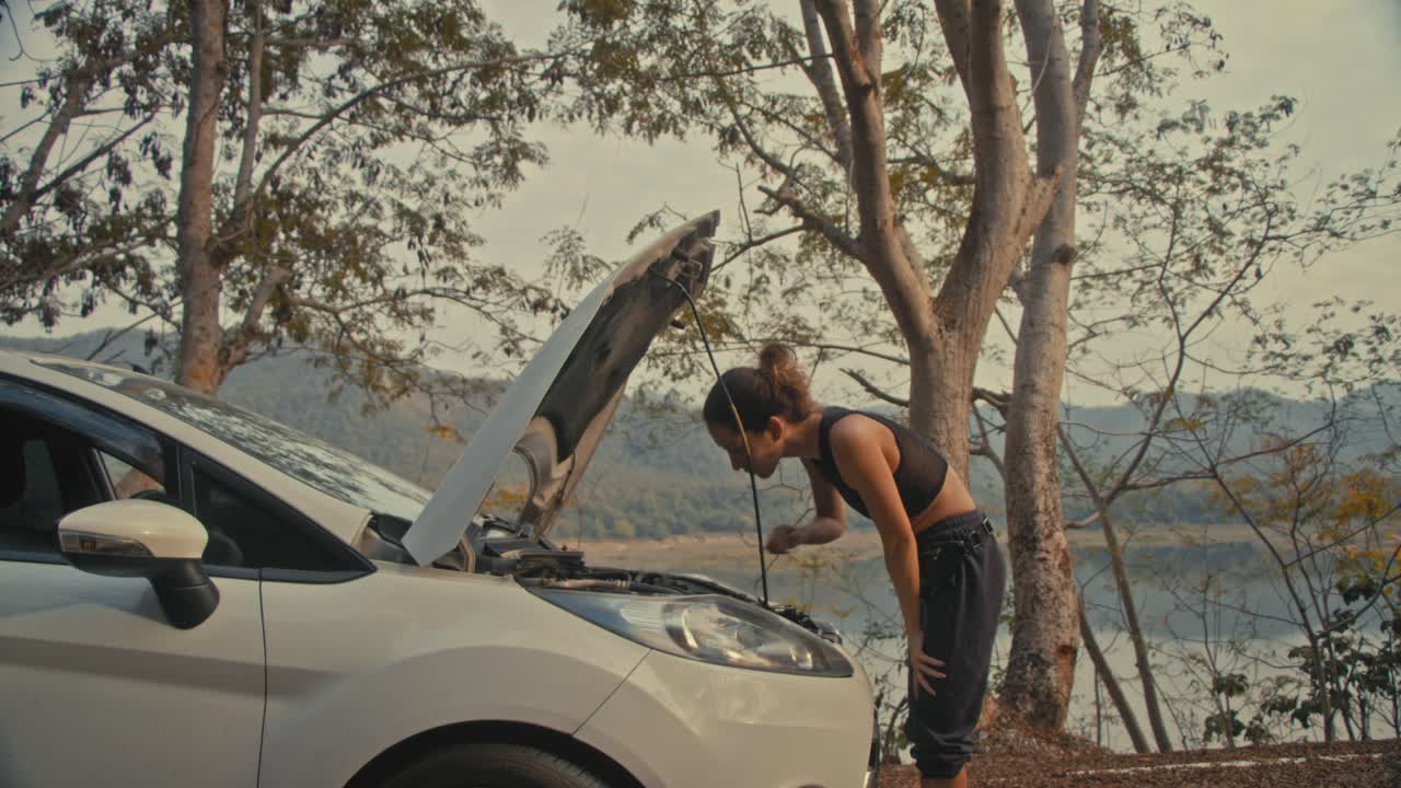 Woman Fixing a Broken Down Car by the Lake