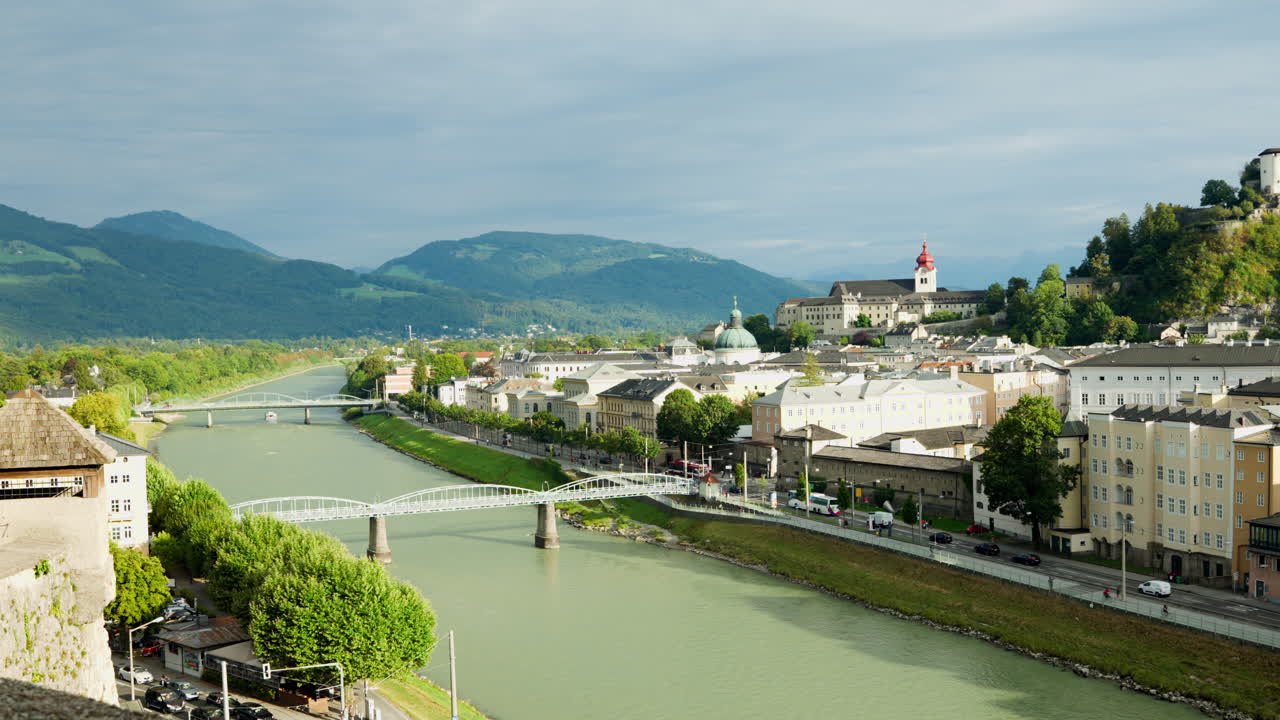 Periferia urbana di Salisburgo, Austria, con una strada che costeggia un canale e montagne verdi sullo sfondo.