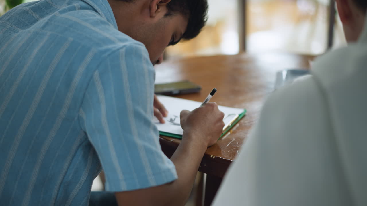 Camera capturing shoulder and hand motion across paper while gripping pen, highlighting smooth drawing movement under soft light with shallow focus on artistic sketch process and body gesture