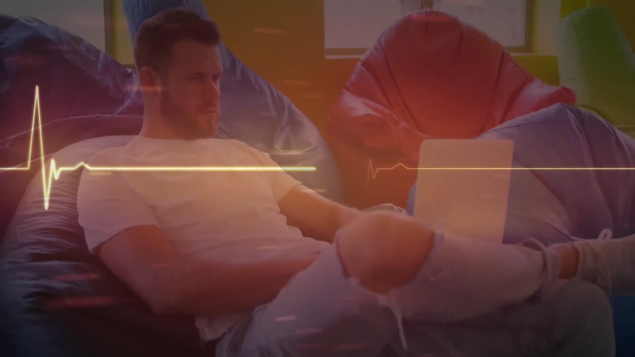 Animation of glowing orange heart rate monitor, over man using laptop