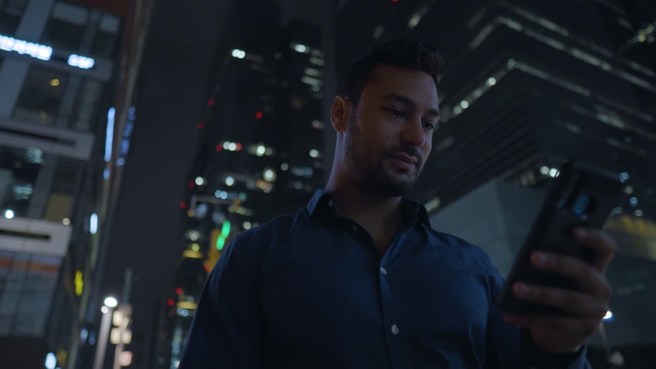 Stylish Man Using Phone at Night Standing Outside Near High Corporate Buildings - push in sliding shot