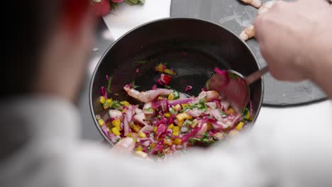 chef prepares cebiche by spooning ingredients into bowl