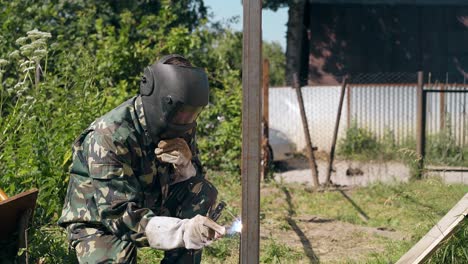 repairman in workwear welds fence carcass at country house