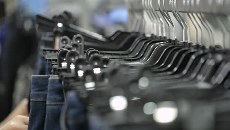 Mujer-En-La-Tienda-Eligiendo-Jeans-Colgados-En-Bastidores