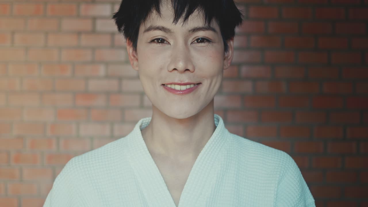 Woman in a robe smiling in front of a brick wall