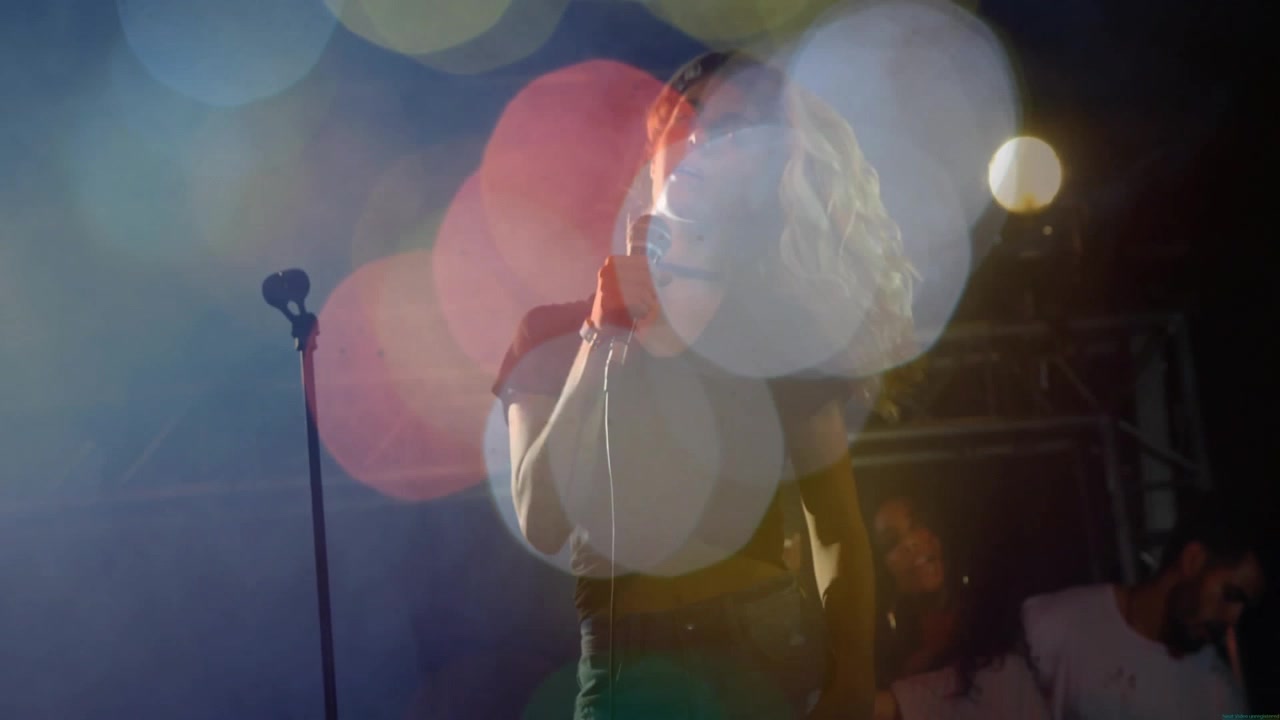 Cantante donna che afferra il microfono e si scuote i capelli tra un bokeh vibrante che fluttua intorno alla band che si esibisce