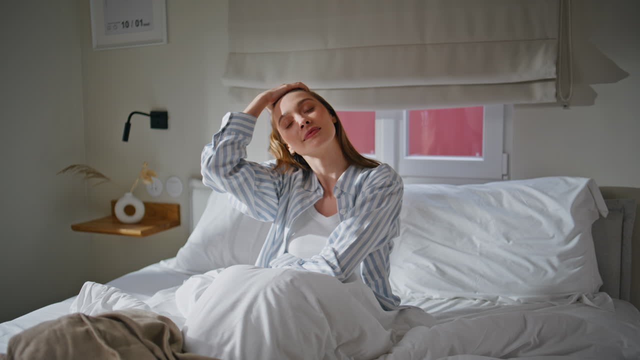 Smiling woman sitting bedding at bedroom enjoying morning. Lady relaxing on bed