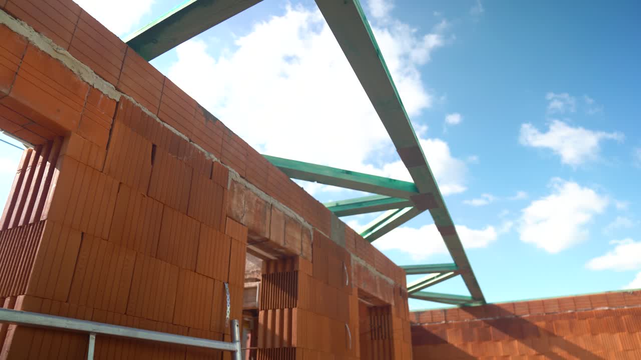 Brick house walls under construction with green timber trusses and blue sky