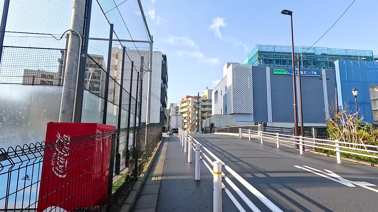 A sunny day stroll along a Tokyo street, showcasing modern buildings and clear skies. Captures urban life and architecture