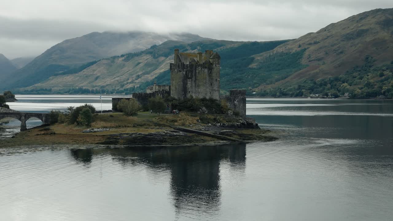 Slow circling aerial of Eilean Donan Castle and reflective lake landscape in the Scottish Highlands