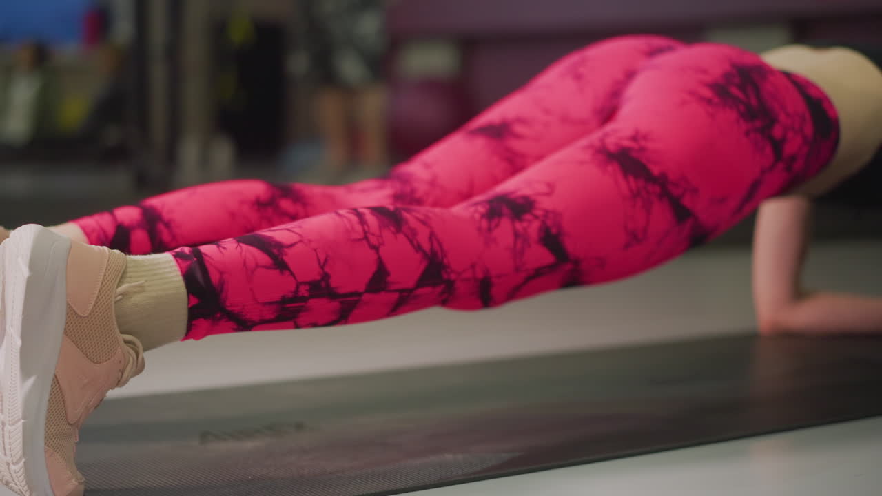 Primo piano dei piedi con le sneakers mentre si fa plank su un tappetino, vista laterale di gambe e busto durante una routine in palestra, tenuta del core focalizzata, allineamento delle caviglie, pavimento dello studio, atmosfera da lezione di gruppo, allenamento di forza progressivo.