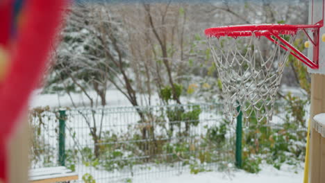 anel de basquete congelado com rede coberta de gelo em primeiro plano, jardim nevado suavemente borrado ao fundo, destacando uma cena de esportes de inverno serena