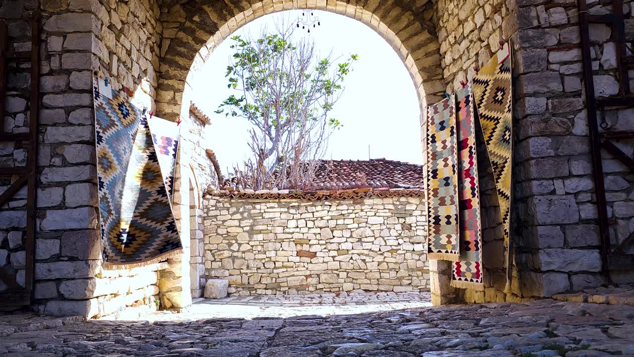 Berat Castle Gate: Welcoming Tourists with Traditional Carpets on Stone Walls in Charming Albanian Destination