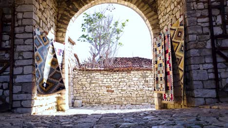 Berat-Castle-Gate:-Welcoming-Tourists-with-Traditional-Carpets-on-Stone-Walls-in-Charming-Albanian-Destination