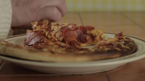 hand grabbing slice of pepperoni pizza close up shot