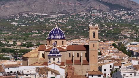 close drone shot orbiting the church of nuestra señora del consuelo in altea, with blue domes, hills, and cityscape