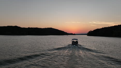 boat riding towards bright orange sunset on arkansas lake, aerial view