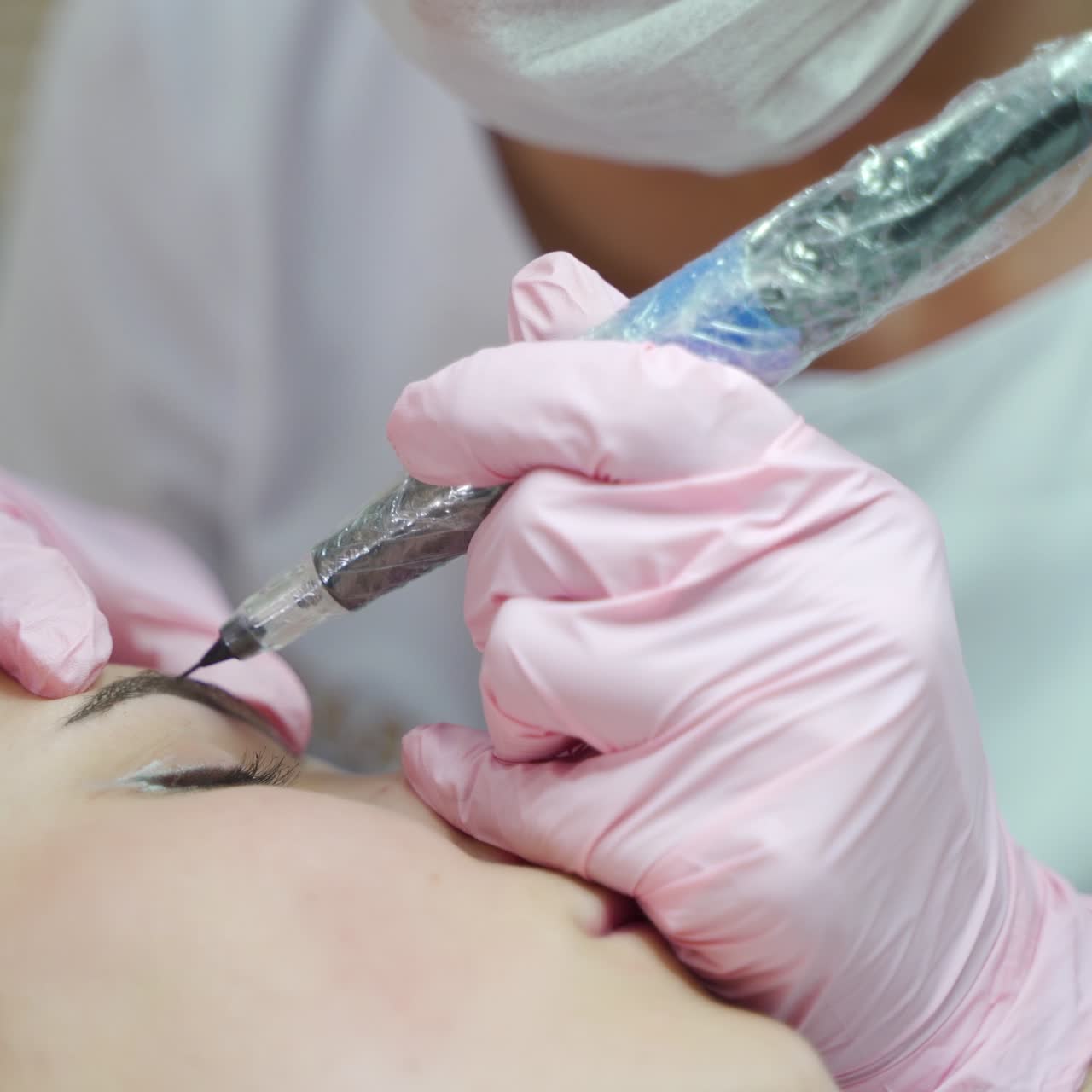 master in gloves is drawing eyebrows to the client with the using of a professional device for permanent makeup of eyebrows. Beauty salon