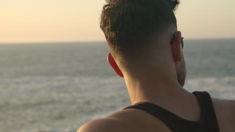 Muscular-man-stranding-on-seashore-at-sunset