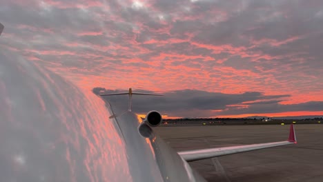 cielo rojo extraordinario al atardecer reflejado en el juselage superior de un jet mientras otro avión aterriza en la parte trasera