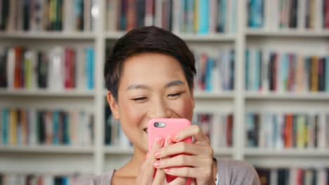 4k video footage of an attractive young woman standing in front of a bookshelf and using a smartphone