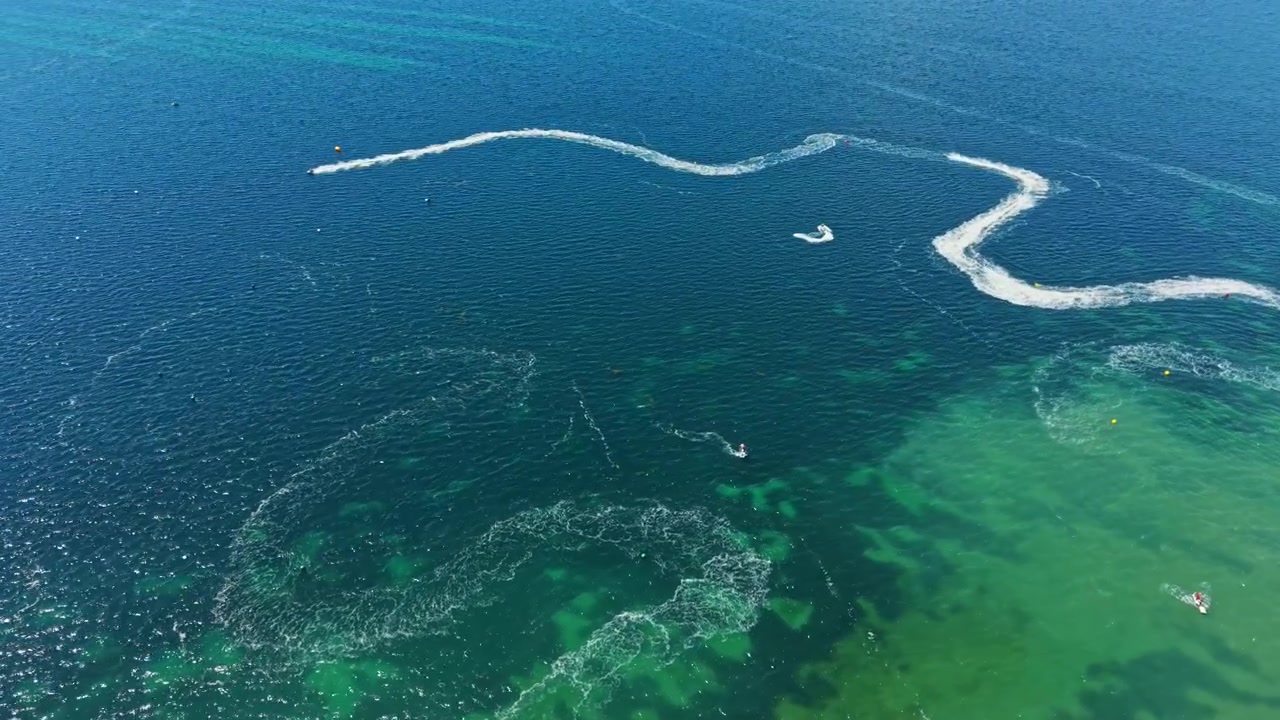 Jet ski racing takes place on a sunny day at a clear coastal location featuring water trails in a vibrant blue ocean