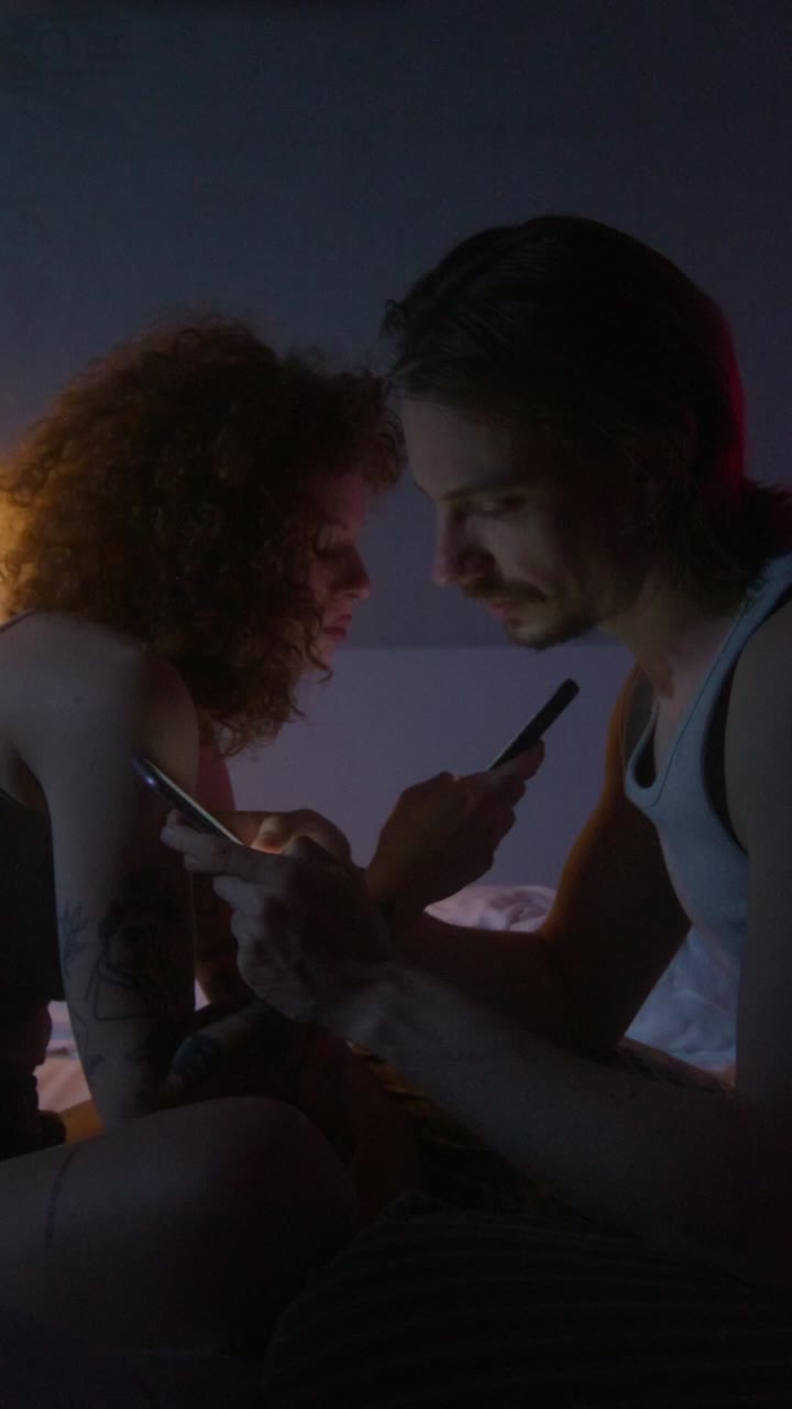 밤에 침실에서 스마트폰을 사용하는 커플