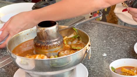 hands serving soup from a hot pot