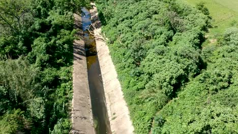 aerial backward view over a drain canal sewer system surrounded by trees and bushes