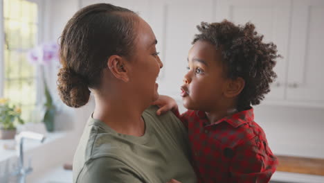 Loving-Mother-Carrying-And-Hugging-Son-At-Home-In-Family-Kitchen