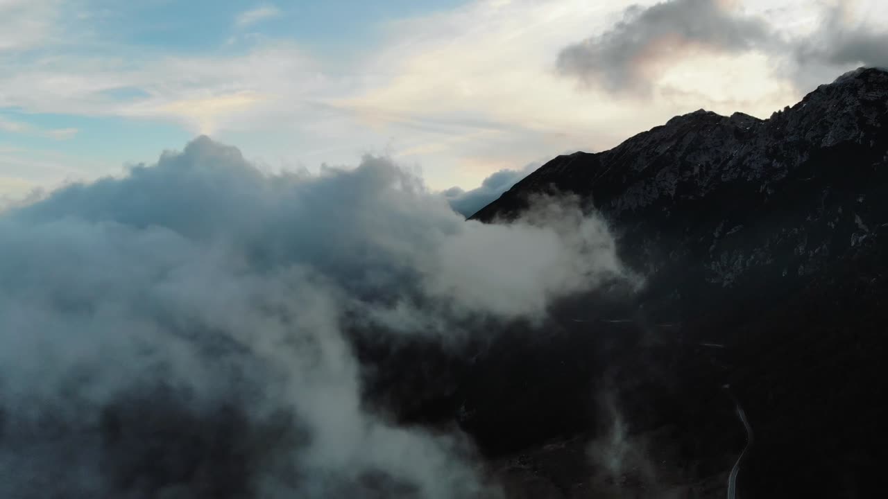 Aerial drone view of mist and clouds drifting around rugged Sierra Nevada peaks with dramatic light and dark mountain slopes creating powerful and mysterious high altitude scenery