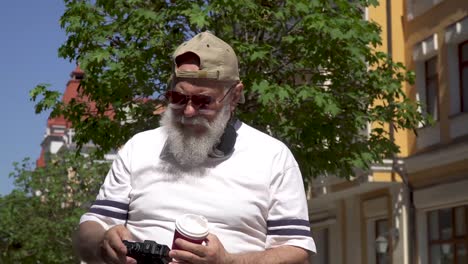 stylish old man in cap and sunglasses take photo walking in the city