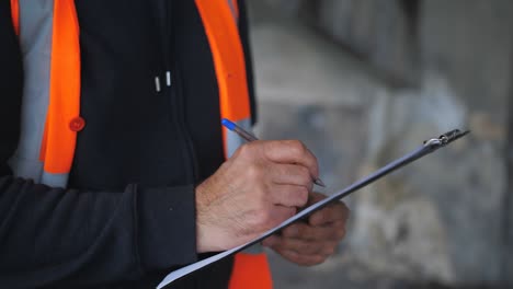 an inspector in a construction helmet records damage to an emergency building in a report.