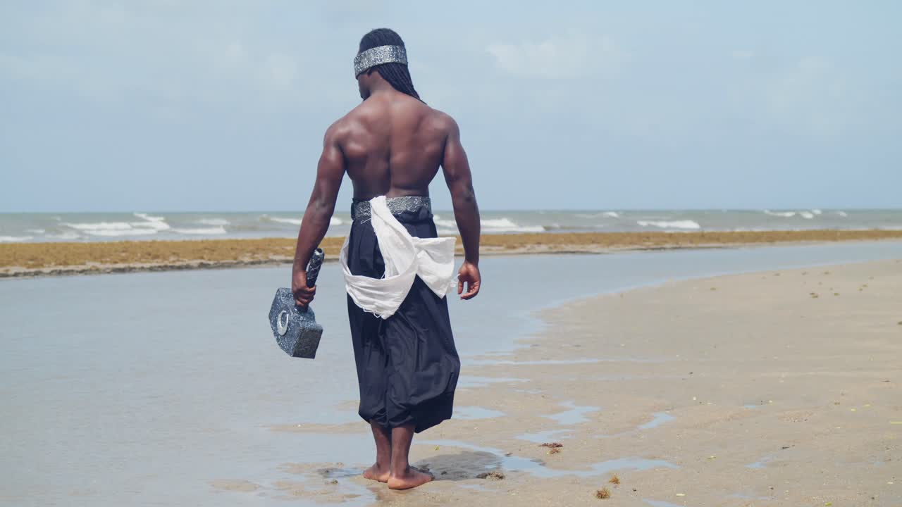 A muscular, dark-skinned man embodies Nekharis cosplay with perfection on a tropical beach