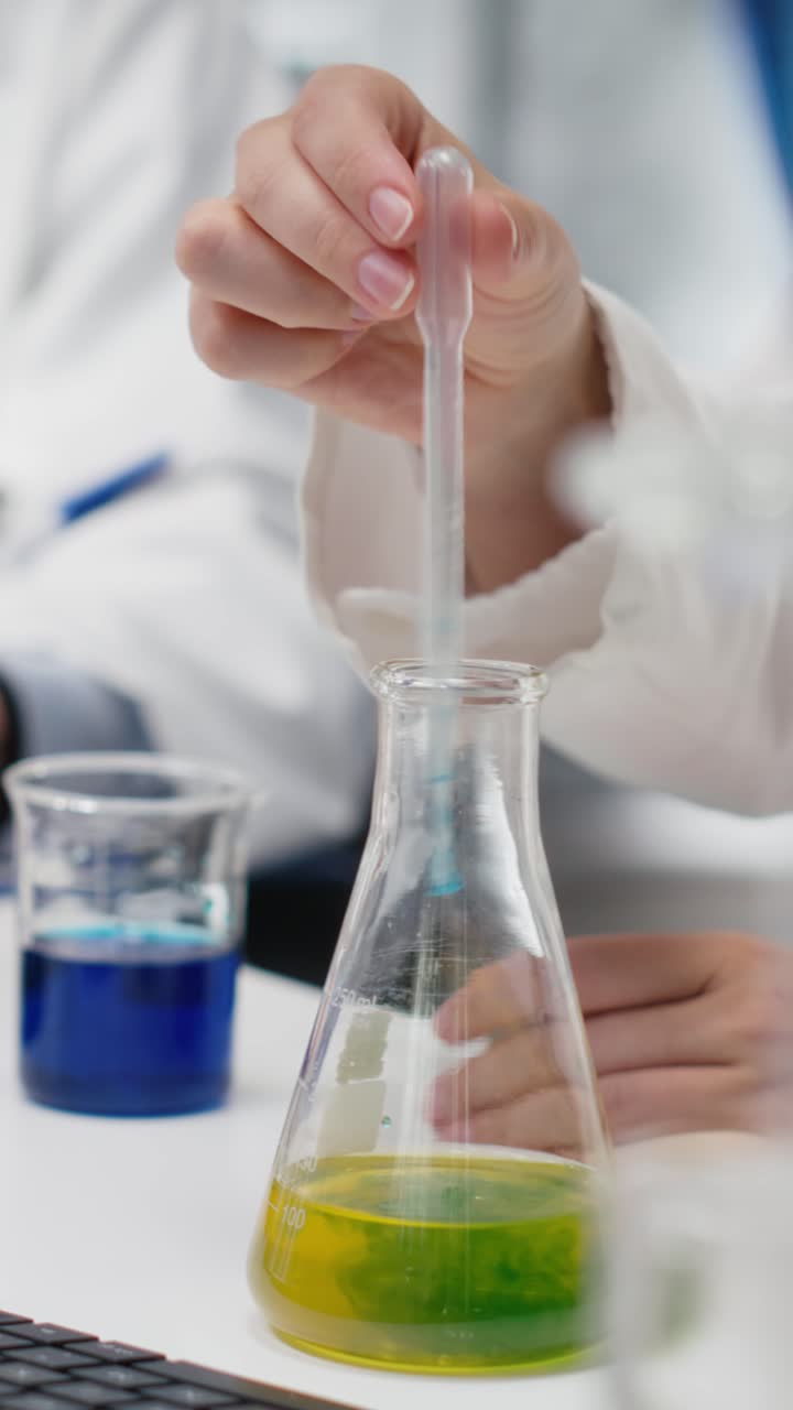 Vertical video Lab manager and trainee shaking glassware filled with green indicator solution