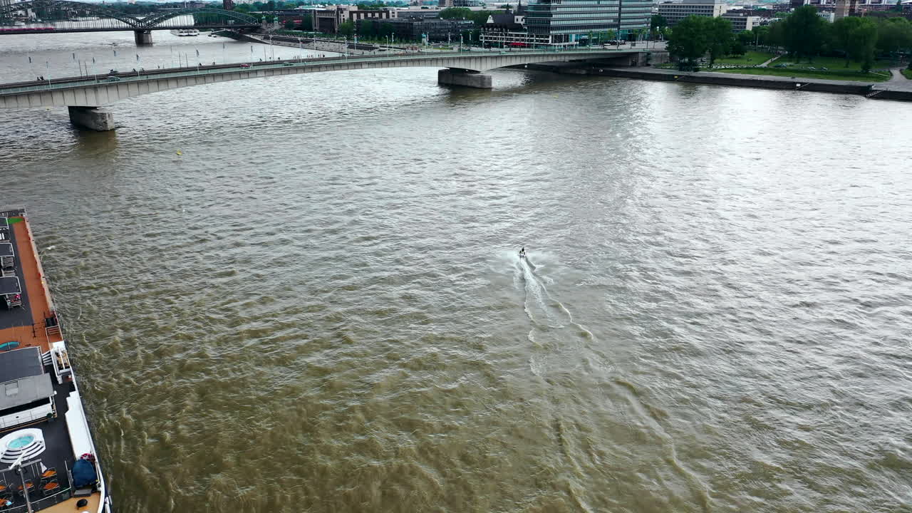A person on a jet ski on a wide river with a bridge and city in the background